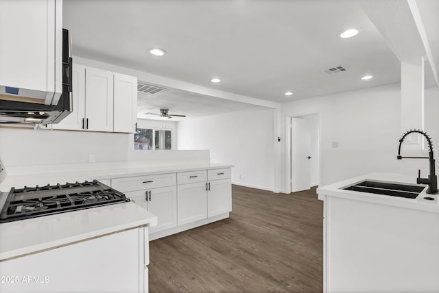 kitchen with a peninsula, a sink, visible vents, white cabinets, and dark wood finished floors