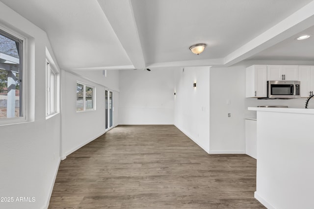 interior space with baseboards, white cabinets, stainless steel microwave, wood finished floors, and beamed ceiling