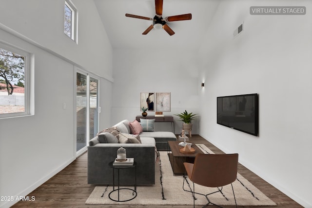 living area with baseboards, a high ceiling, visible vents, and wood finished floors