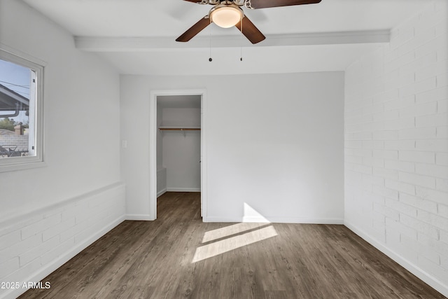 unfurnished bedroom featuring brick wall, baseboards, beam ceiling, and wood finished floors