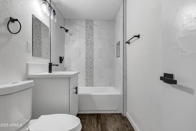 bathroom with a textured wall, toilet, wood finished floors, vanity, and washtub / shower combination