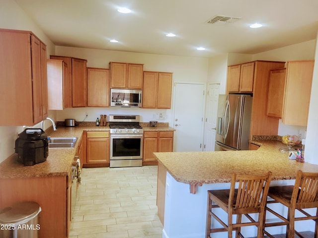 kitchen featuring visible vents, a peninsula, a breakfast bar, a sink, and stainless steel appliances