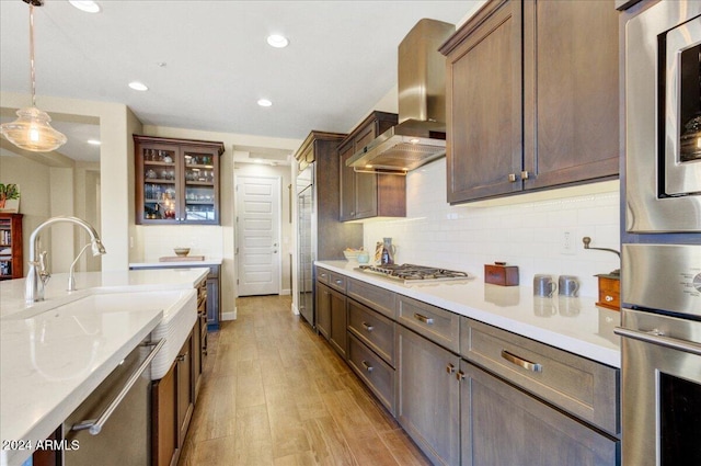 kitchen with pendant lighting, wall chimney range hood, light hardwood / wood-style flooring, light stone countertops, and stainless steel appliances