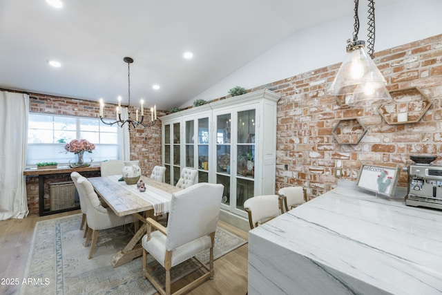 dining space with vaulted ceiling, brick wall, a chandelier, and light hardwood / wood-style flooring