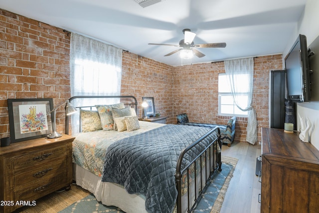 bedroom featuring hardwood / wood-style flooring, ceiling fan, and brick wall