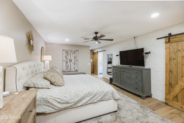 bedroom featuring hardwood / wood-style flooring, ceiling fan, brick wall, and a barn door