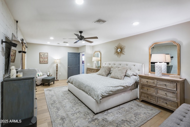 bedroom featuring a barn door, ceiling fan, and light wood-type flooring