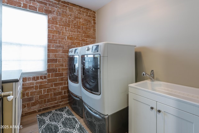 washroom featuring cabinets, brick wall, washer and clothes dryer, and light wood-type flooring