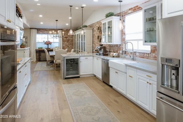 kitchen with appliances with stainless steel finishes, wine cooler, light stone countertops, white cabinets, and decorative light fixtures