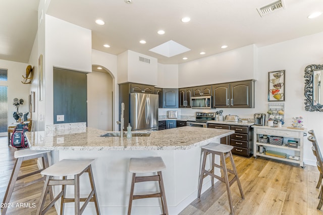 kitchen with dark brown cabinets, a kitchen bar, appliances with stainless steel finishes, and light hardwood / wood-style floors