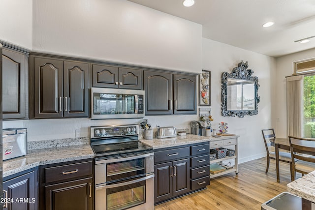 kitchen with dark brown cabinets, light wood-type flooring, stainless steel appliances, and light stone counters