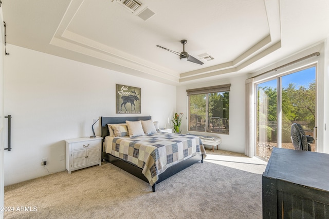 carpeted bedroom featuring ceiling fan, access to exterior, and a tray ceiling