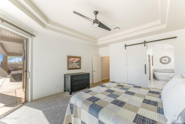 carpeted bedroom with a barn door, ceiling fan, a tray ceiling, and connected bathroom