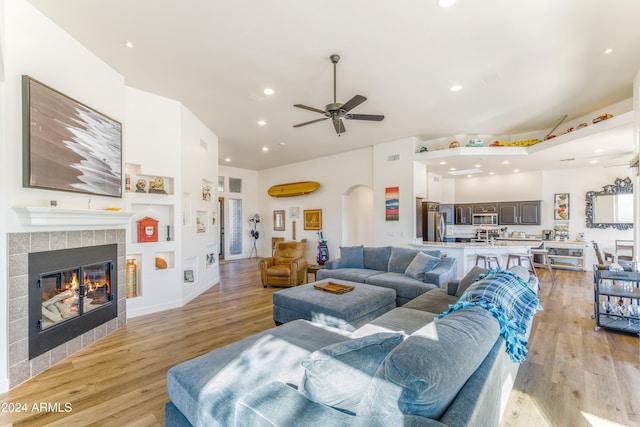 living room with light wood-type flooring, a tile fireplace, and ceiling fan