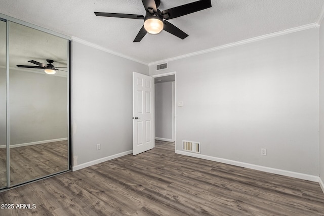 unfurnished bedroom featuring visible vents, a textured ceiling, wood finished floors, a closet, and crown molding