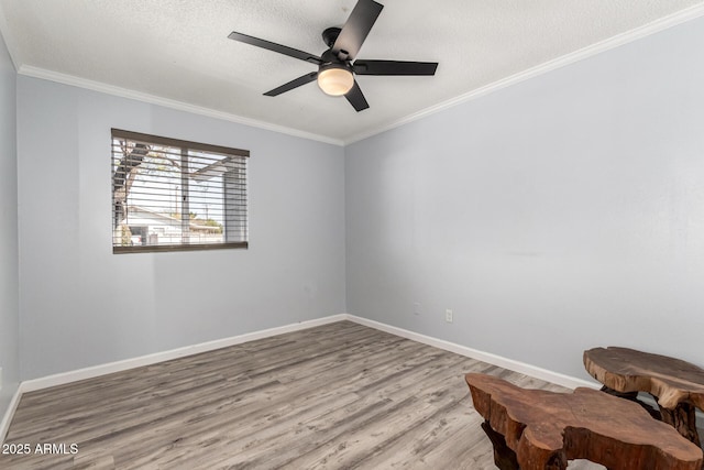 empty room with a ceiling fan, a textured ceiling, wood finished floors, crown molding, and baseboards