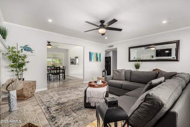 living room with visible vents, wood finished floors, baseboards, and ornamental molding