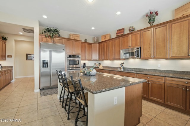 kitchen with a breakfast bar area, appliances with stainless steel finishes, dark stone countertops, a center island, and light tile patterned flooring