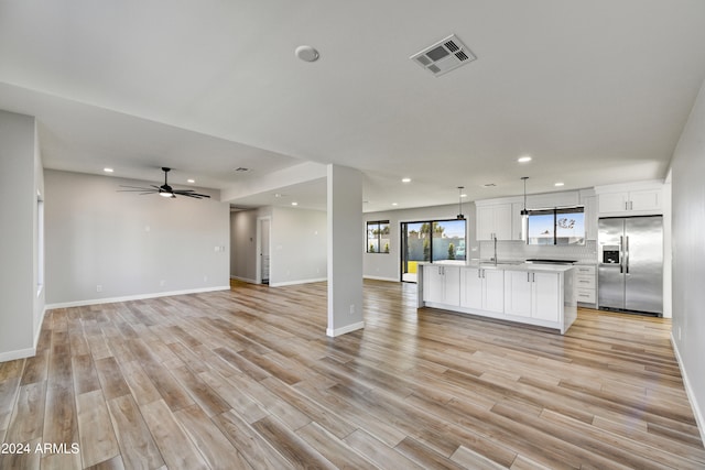 kitchen with light wood-type flooring, pendant lighting, a center island with sink, white cabinets, and stainless steel fridge with ice dispenser