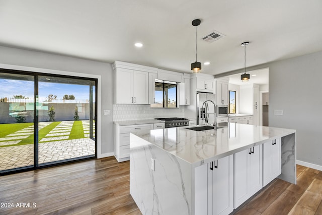 kitchen featuring hanging light fixtures, light stone counters, wood-type flooring, a center island with sink, and white cabinets