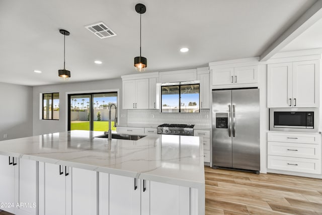 kitchen with light stone countertops, appliances with stainless steel finishes, sink, white cabinetry, and an island with sink