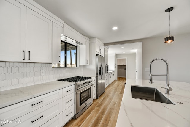 kitchen featuring white cabinetry, sink, hanging light fixtures, light hardwood / wood-style flooring, and appliances with stainless steel finishes