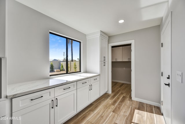 kitchen with light stone counters, white cabinetry, and light hardwood / wood-style flooring