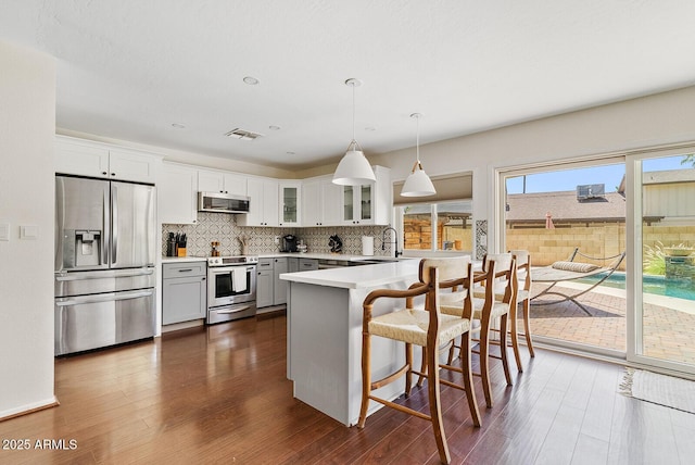 5912 E Wethersfield Rd, Scottsdale, AZ 85254 - kitchen featuring stainless steel appliances, dark wood-style flooring, glass insert cabinets, a peninsula, and backsplash