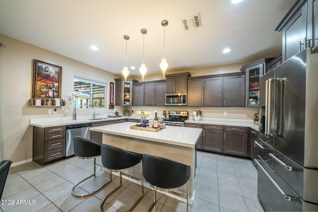 kitchen with pendant lighting, appliances with stainless steel finishes, dark brown cabinets, a kitchen island, and a breakfast bar area