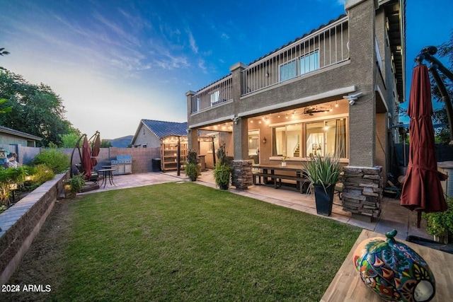 back house at dusk featuring a lawn, a patio area, and a balcony