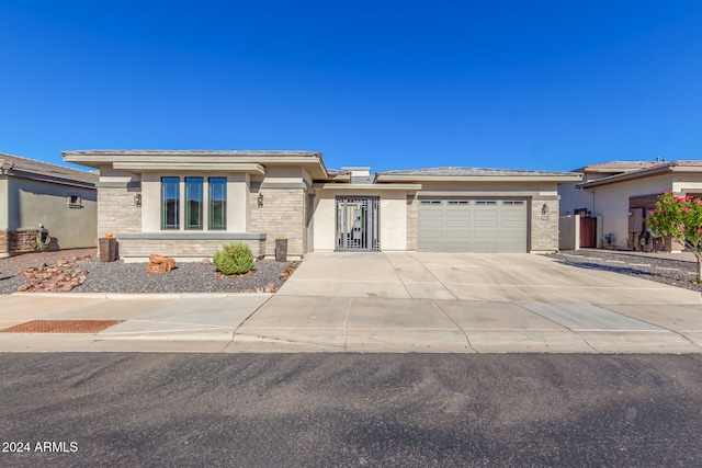 prairie-style home with driveway, stone siding, a garage, and stucco siding