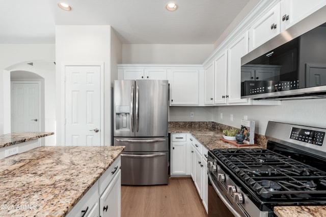 kitchen featuring stainless steel appliances, white cabinets, light wood-style floors, arched walkways, and light stone counters