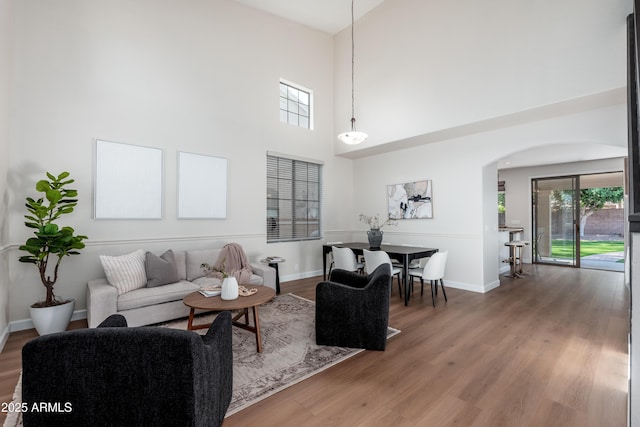 living area featuring arched walkways, a towering ceiling, healthy amount of natural light, and wood finished floors