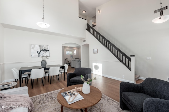 living room with arched walkways, stairs, wood finished floors, a high ceiling, and baseboards