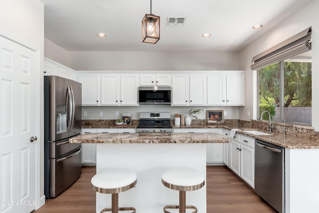kitchen featuring stainless steel appliances, a sink, white cabinetry, wood finished floors, and recessed lighting