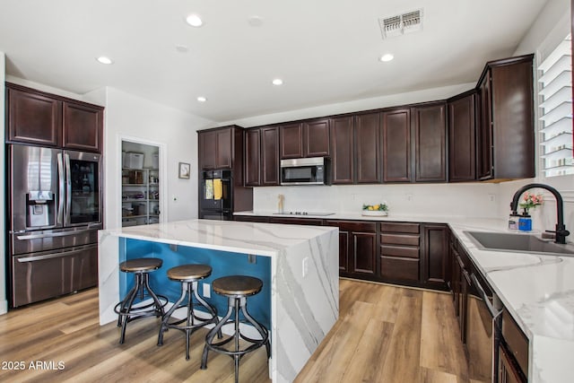 kitchen with light stone countertops, a kitchen island, sink, and black appliances