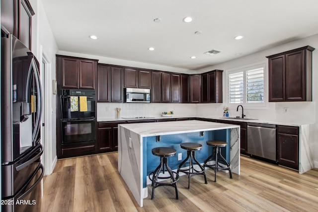 kitchen featuring a breakfast bar, sink, a center island, black appliances, and light hardwood / wood-style flooring