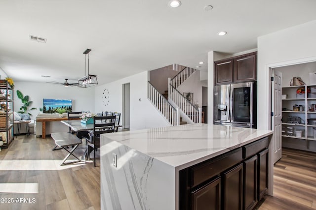 kitchen with light hardwood / wood-style flooring, dark brown cabinets, a center island, stainless steel fridge with ice dispenser, and decorative light fixtures