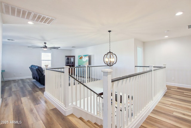 stairway featuring hardwood / wood-style flooring and ceiling fan with notable chandelier