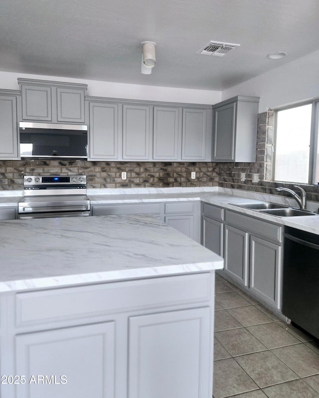 kitchen with a sink, decorative backsplash, appliances with stainless steel finishes, and gray cabinetry