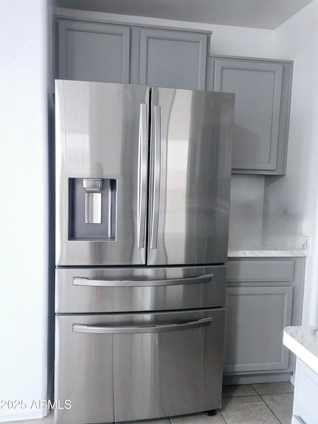 kitchen featuring stainless steel fridge, light tile patterned floors, gray cabinetry, and light stone counters