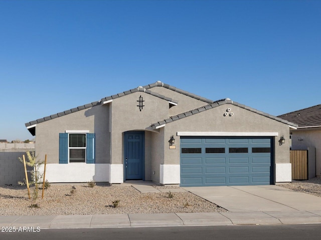 view of front of house featuring a tile roof, stucco siding, fence, driveway, and a garage