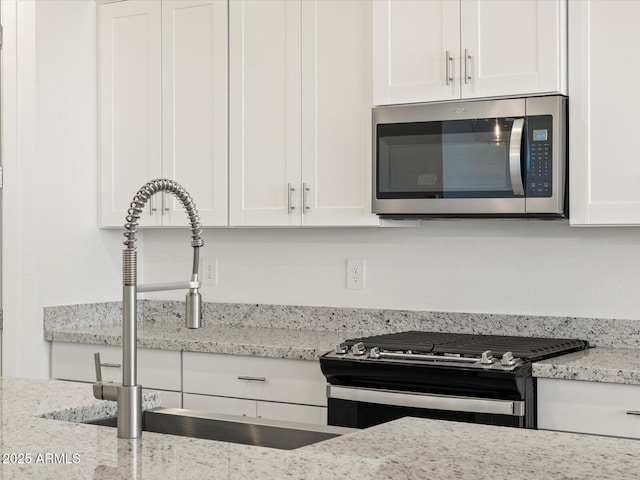 kitchen featuring a sink, white cabinets, light stone countertops, and appliances with stainless steel finishes