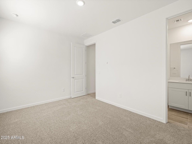 unfurnished room featuring baseboards, visible vents, a sink, and light carpet