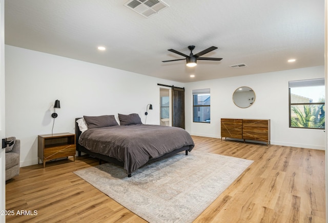 bedroom with visible vents, light wood-style flooring, baseboards, and a barn door