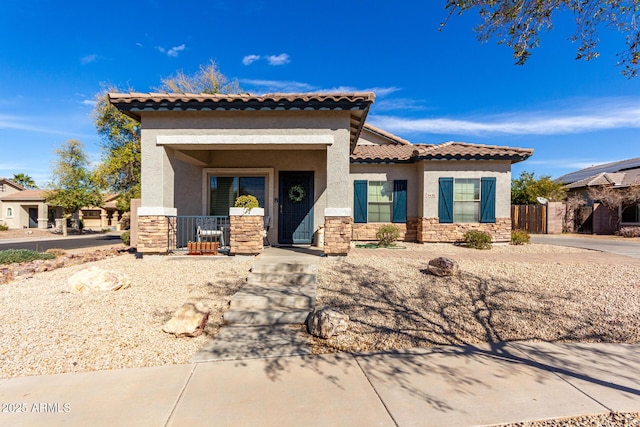 mediterranean / spanish home with stone siding, a tile roof, and stucco siding