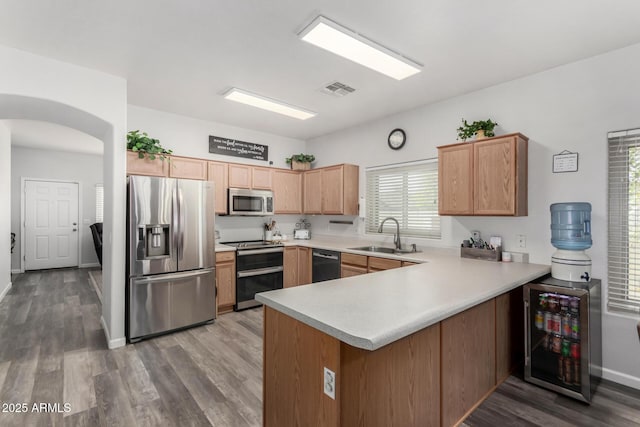 kitchen with arched walkways, wine cooler, a peninsula, a sink, and appliances with stainless steel finishes