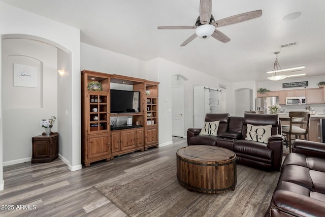 living room featuring arched walkways, visible vents, a barn door, ceiling fan, and wood finished floors