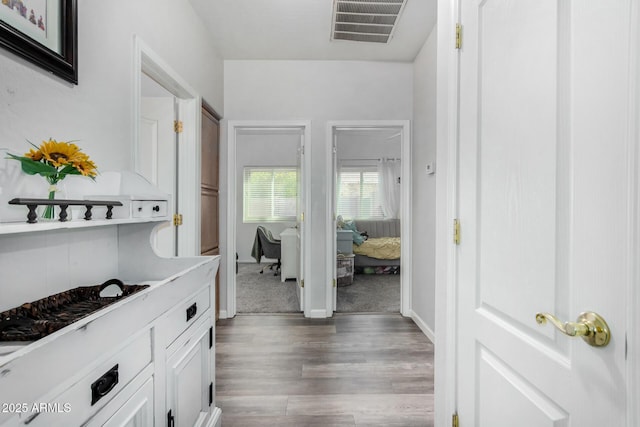 hallway with baseboards, visible vents, and wood finished floors