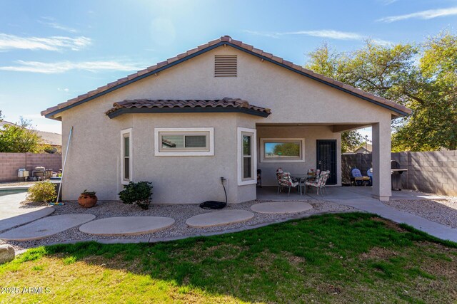 rear view of property with a tiled roof, fence, a yard, a patio area, and stucco siding